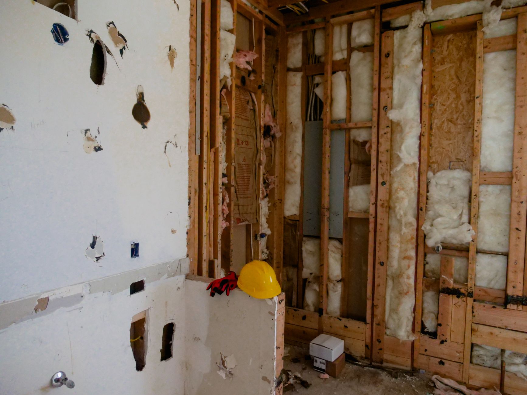 A stripped interior room mid-renovation, with bare studs, exposed subfloor and debris on the ground