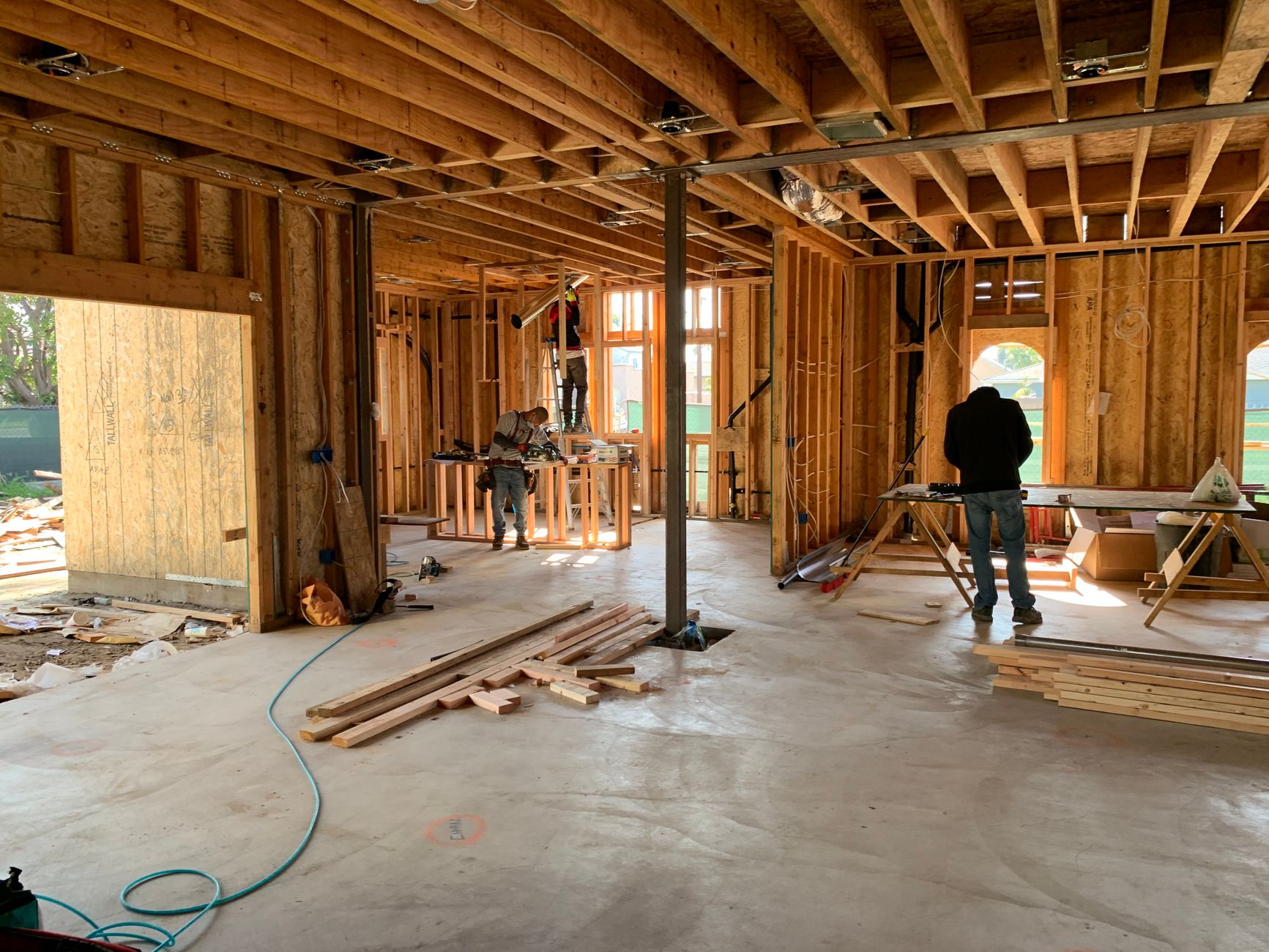 Workers inside a house at the framing stage, with open stud walls and ceiling joists still visible