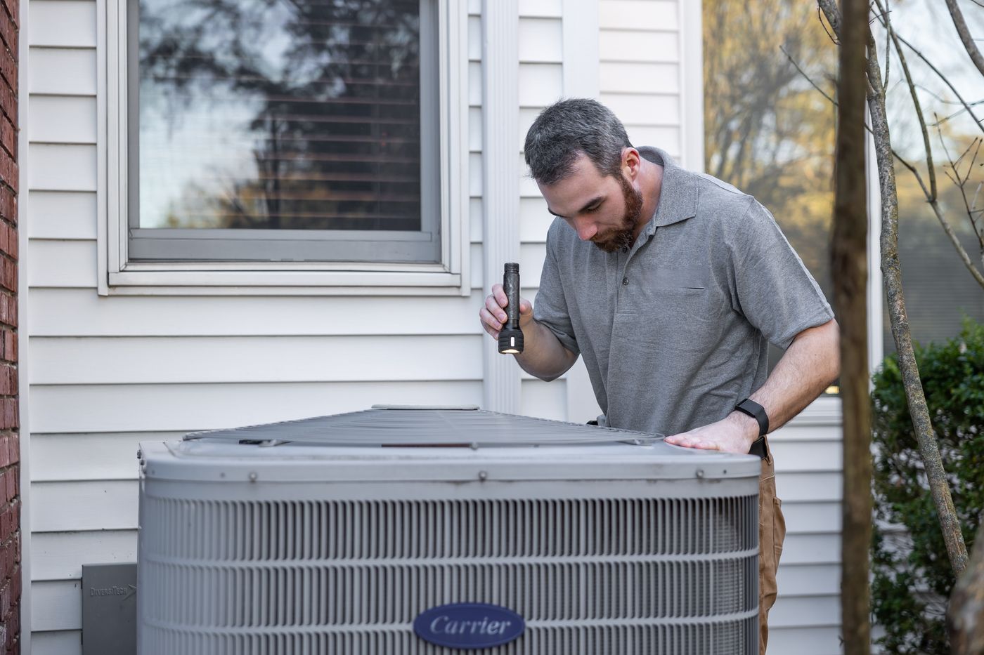 A technician inspecting an outdoor air conditioning unit beside a building