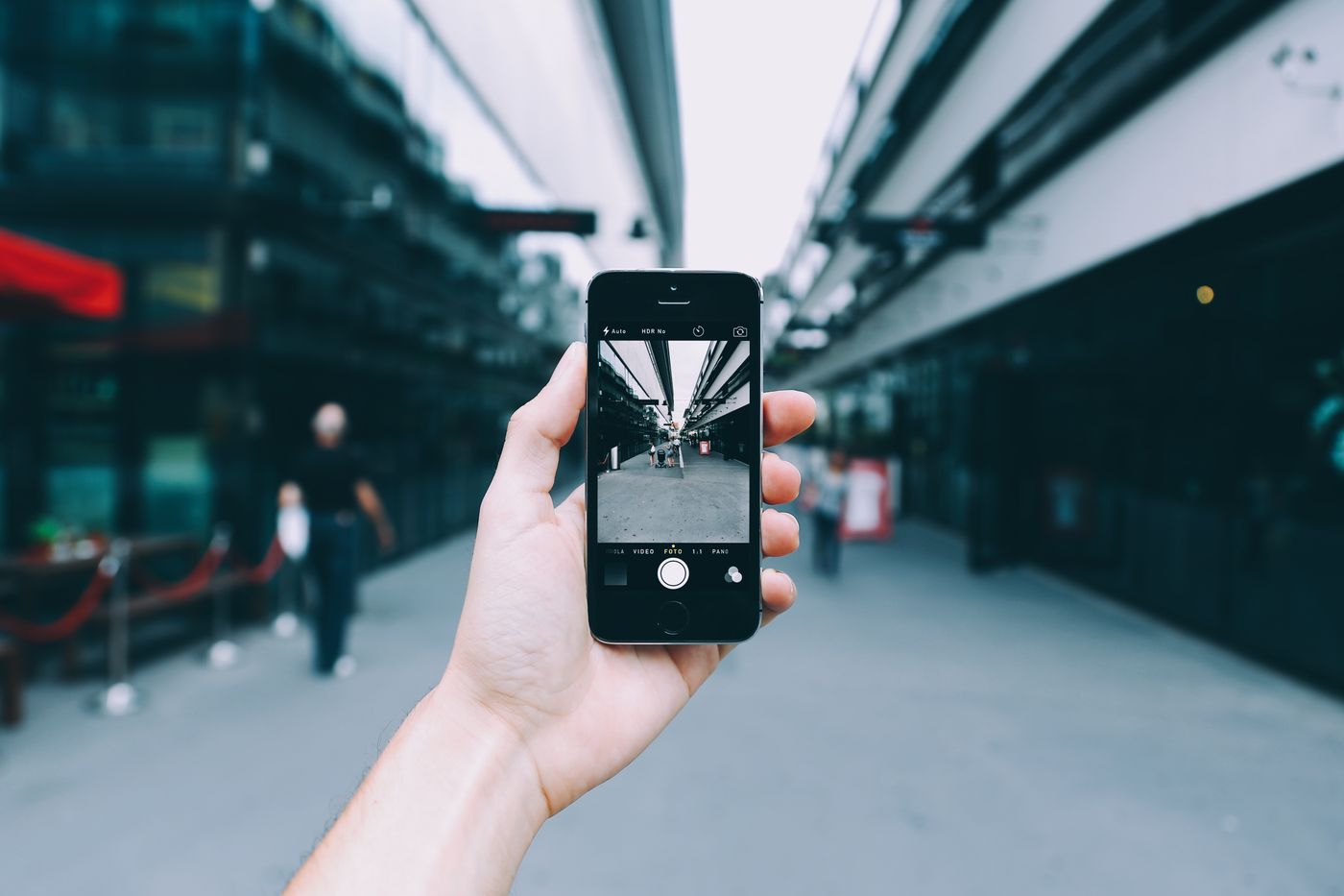 A hand holding a smartphone, taking a photo of a city street under a bridge.