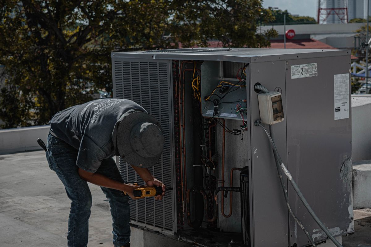 A technician repairing a rooftop air-conditioning unit during a maintenance call.