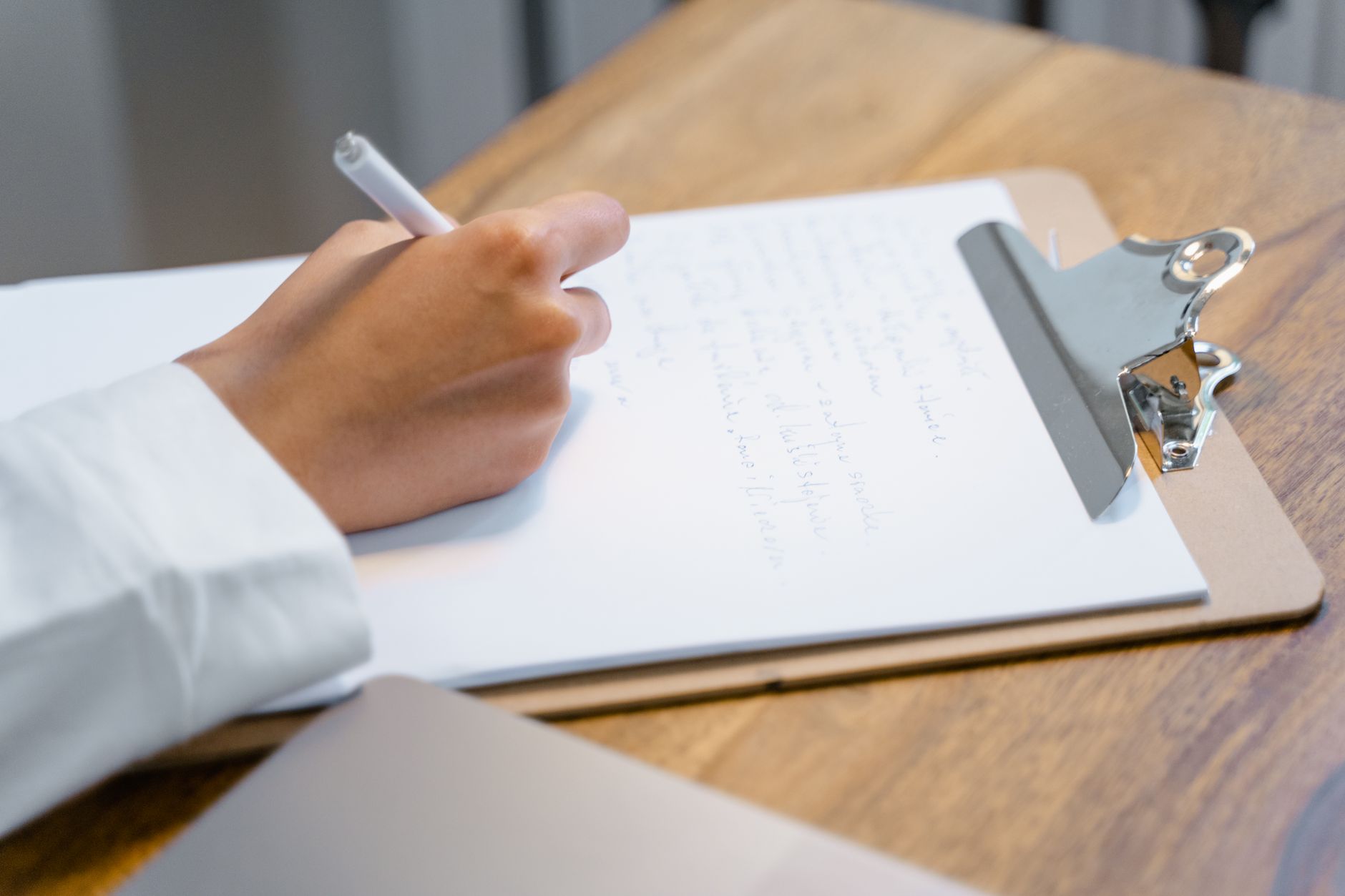 A close-up of a hand writing on a clipboard resting on a wooden table