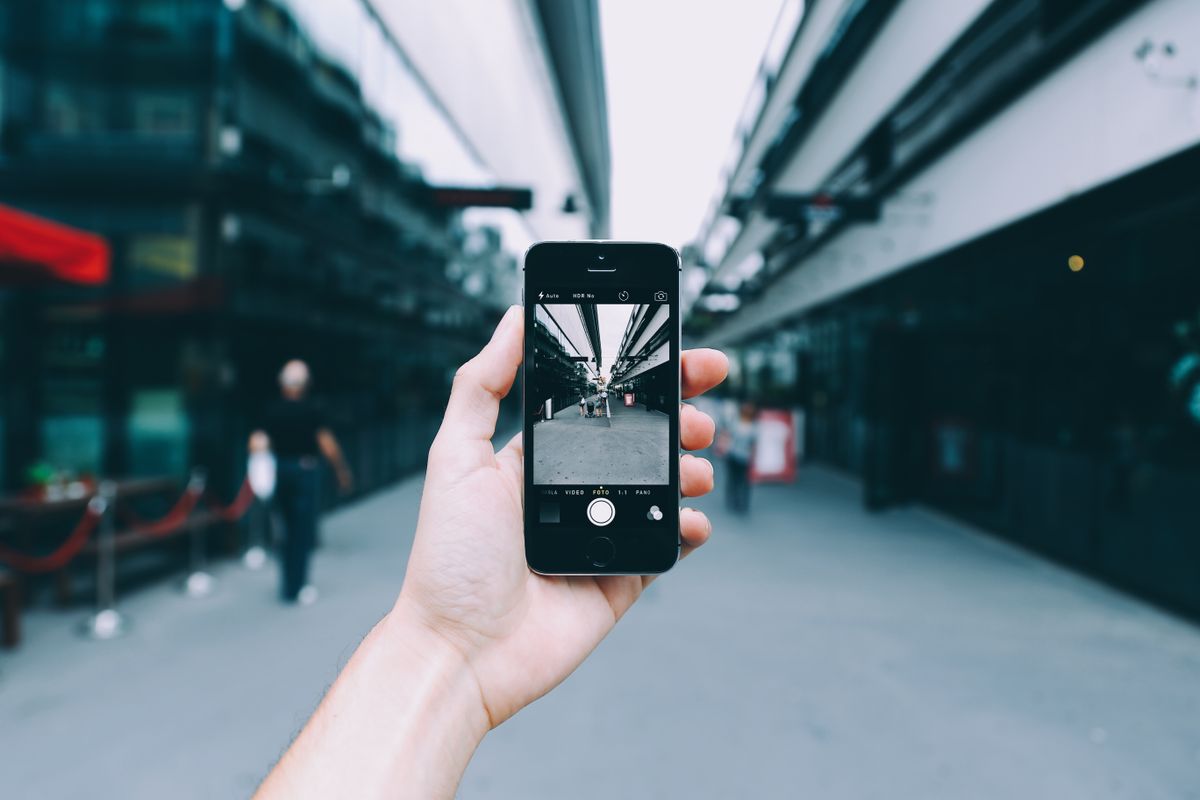 A hand holding a phone, taking a photo of a street scene